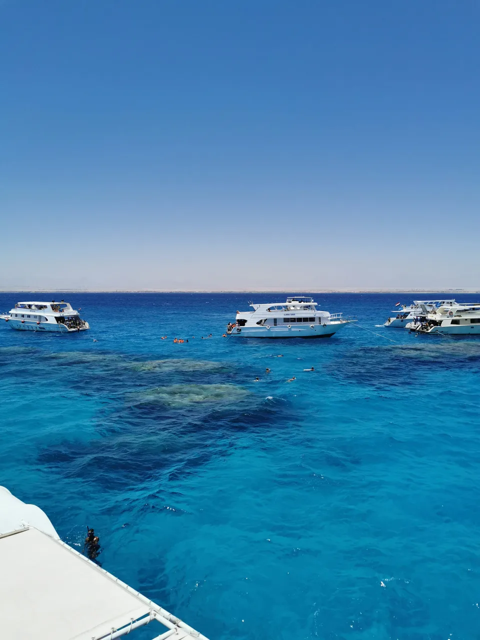 Boats floating on clear turquoise water beneath a blue sky