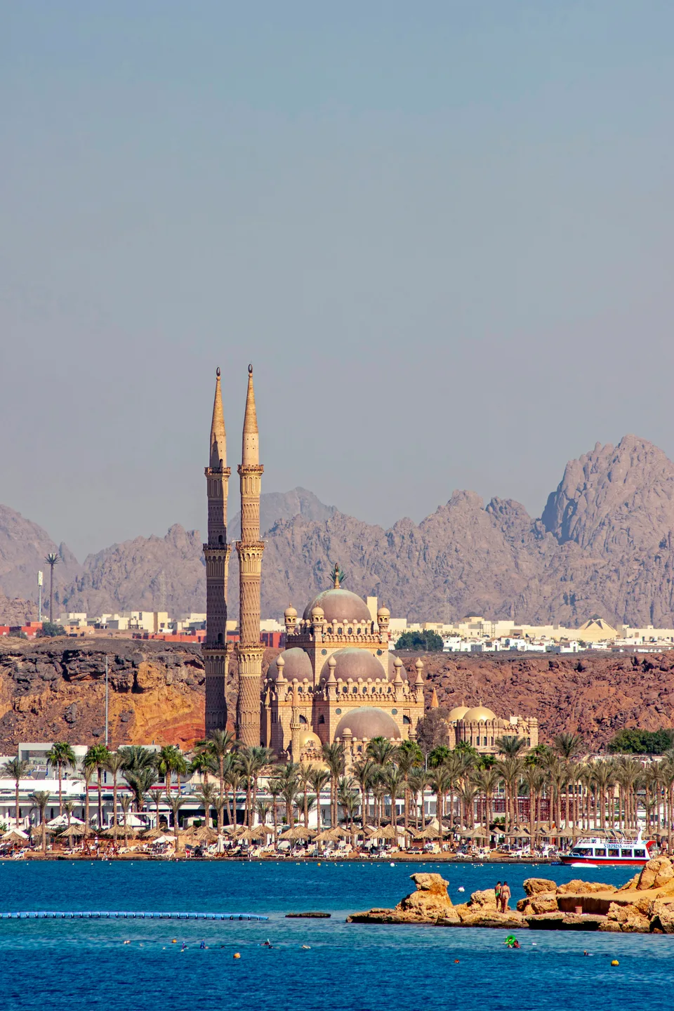 Mosque minarets above a coastal harbour with mountains beyond