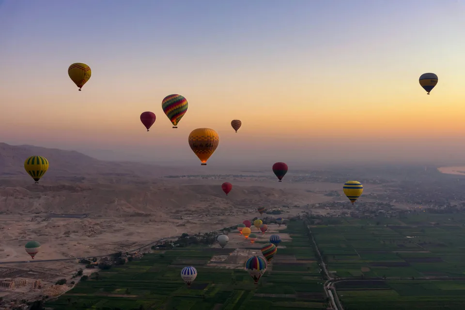 Hot air balloons above green fields and desert at sunrise