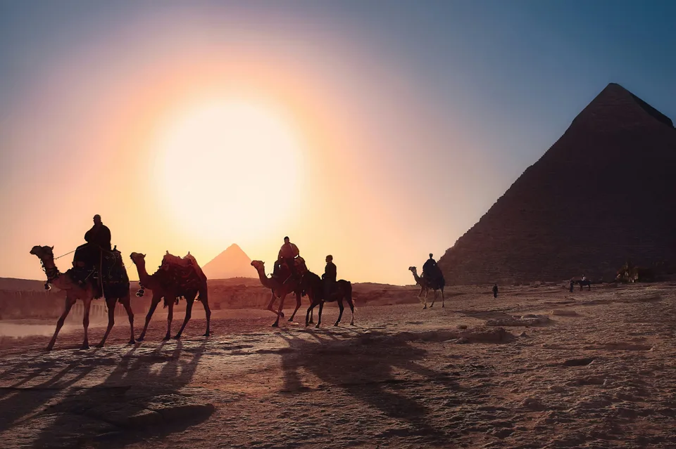 Camel riders silhouetted against the sunset near a pyramid