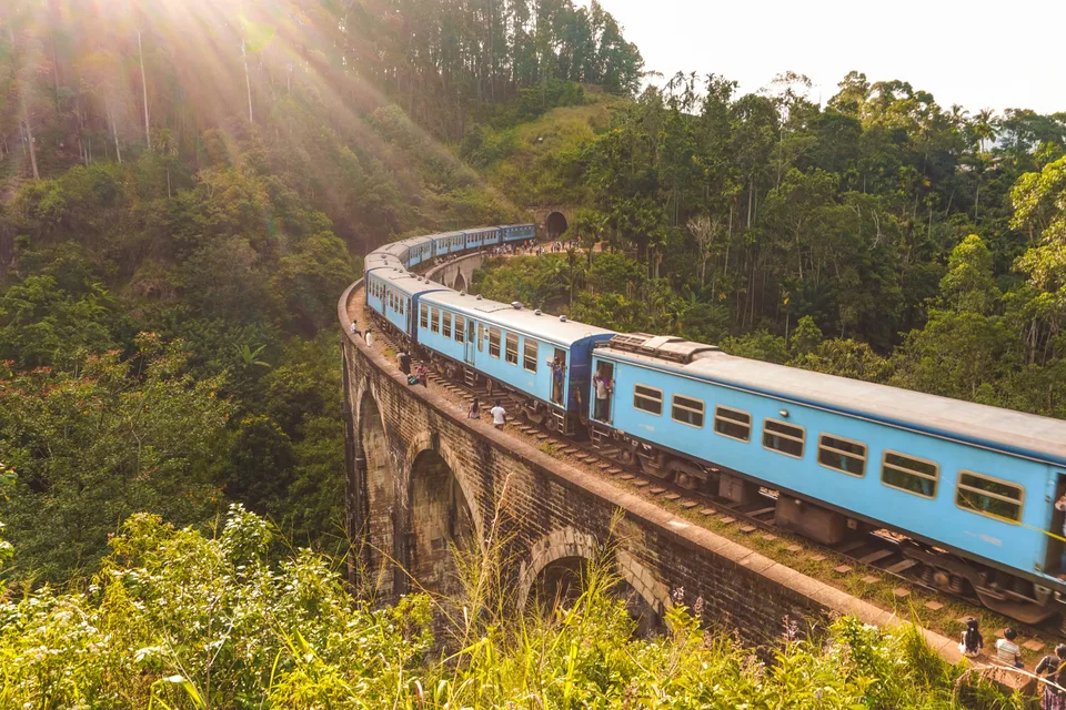 A train curving over a bridge through sunlit green hills