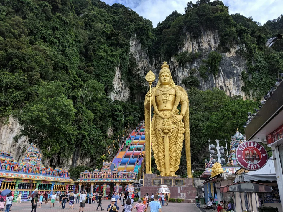 Golden statue and colourful temple steps below limestone cliffs at Batu Caves
