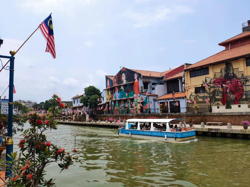 Malaysian flag and a boat beside historic riverside buildings