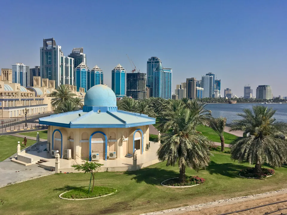 Blue-domed pavilion and palms beside the Sharjah skyline