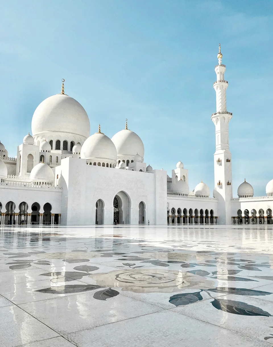White mosque domes above a marble courtyard under blue skies