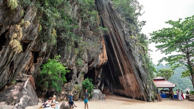 Visitors on the beach below the leaning cliffs of Khao Phing Kan in Phang Nga Bay