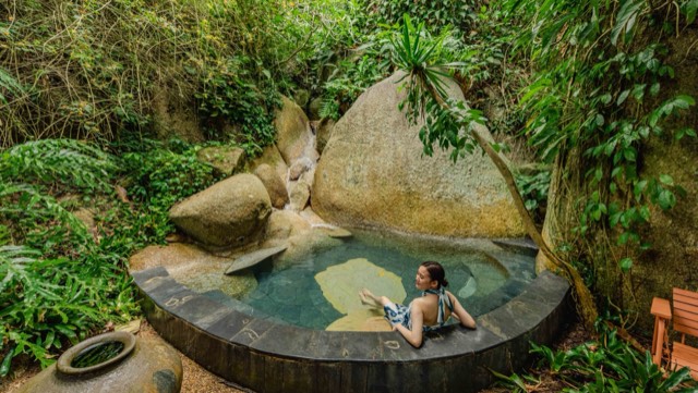 A guest relaxing in a stone pool surrounded by tropical forest on Ko Samui
