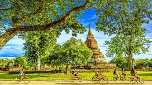 Cyclists passing a brick chedi under trees in Sukhothai Historical Park