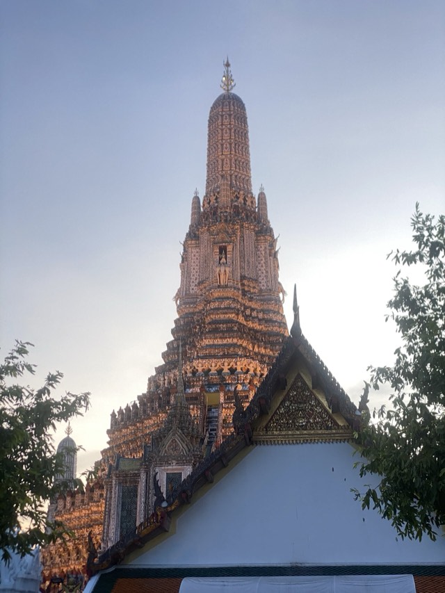The central prang of Wat Arun rising above a temple roof at sunset in Bangkok