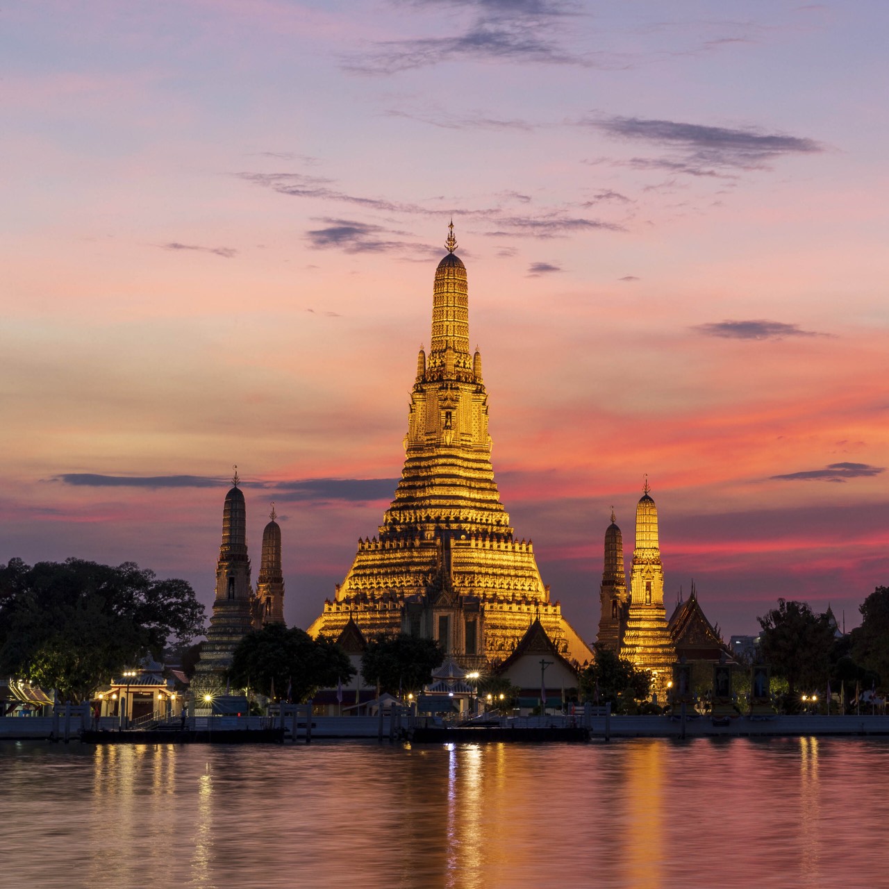 Wat Arun reflected in the Chao Phraya river under a pink sunset sky in Bangkok